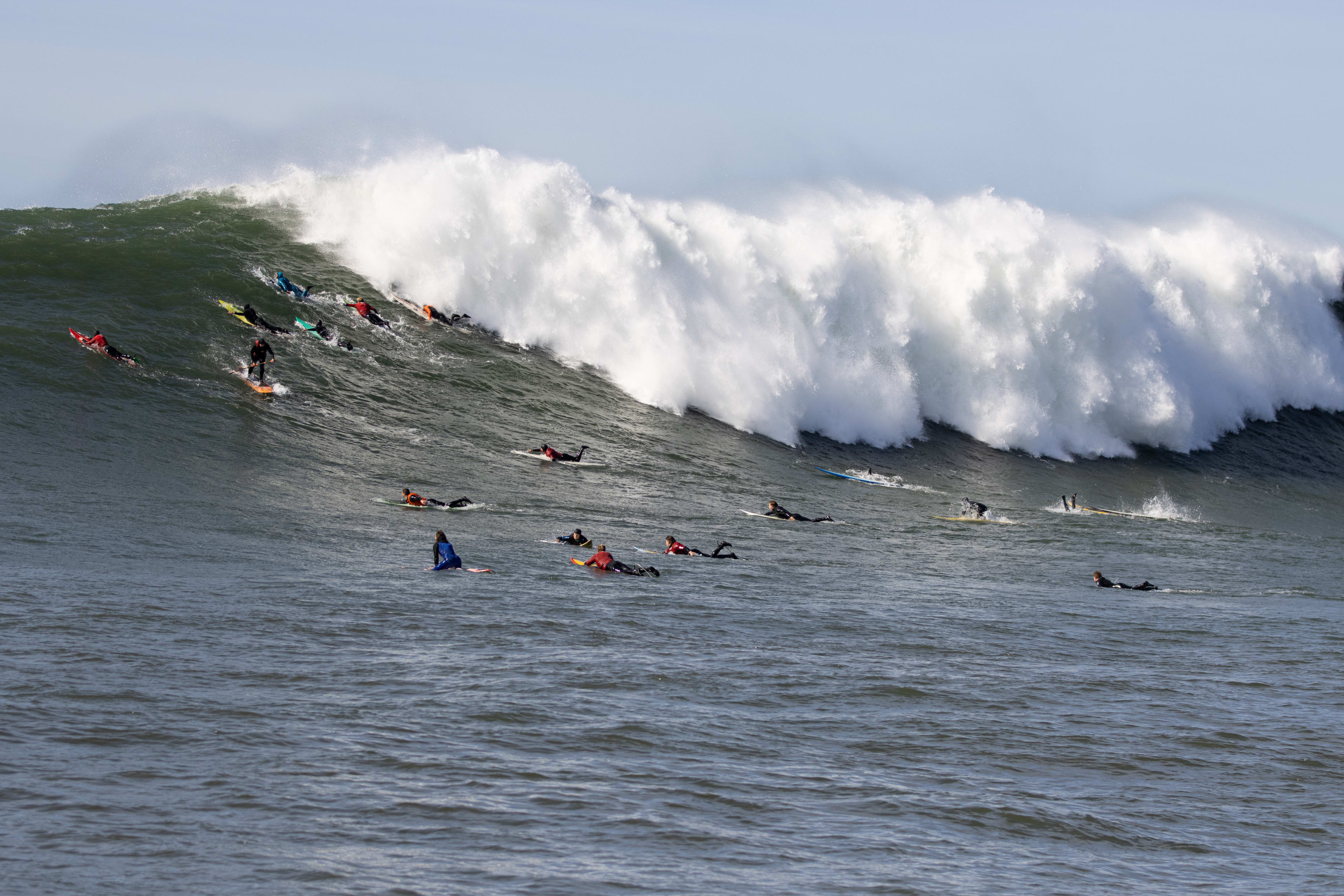 A large wave at Mavericks cleans up a crowd of surfers.